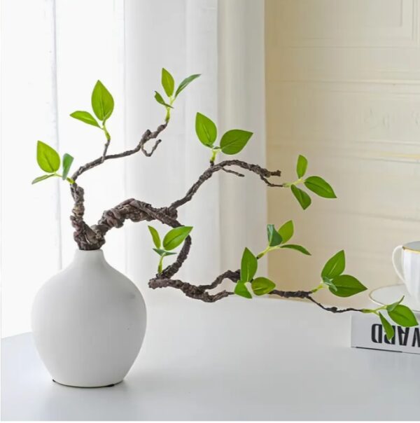 กิ่งไม้ฟิกัสเทียมที่เหมือนจริงในแจกันเซรามิกสีขาว